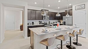 Una cocina moderna con gabinetes oscuros, una isla grande con taburetes de bar e iluminación colgante.