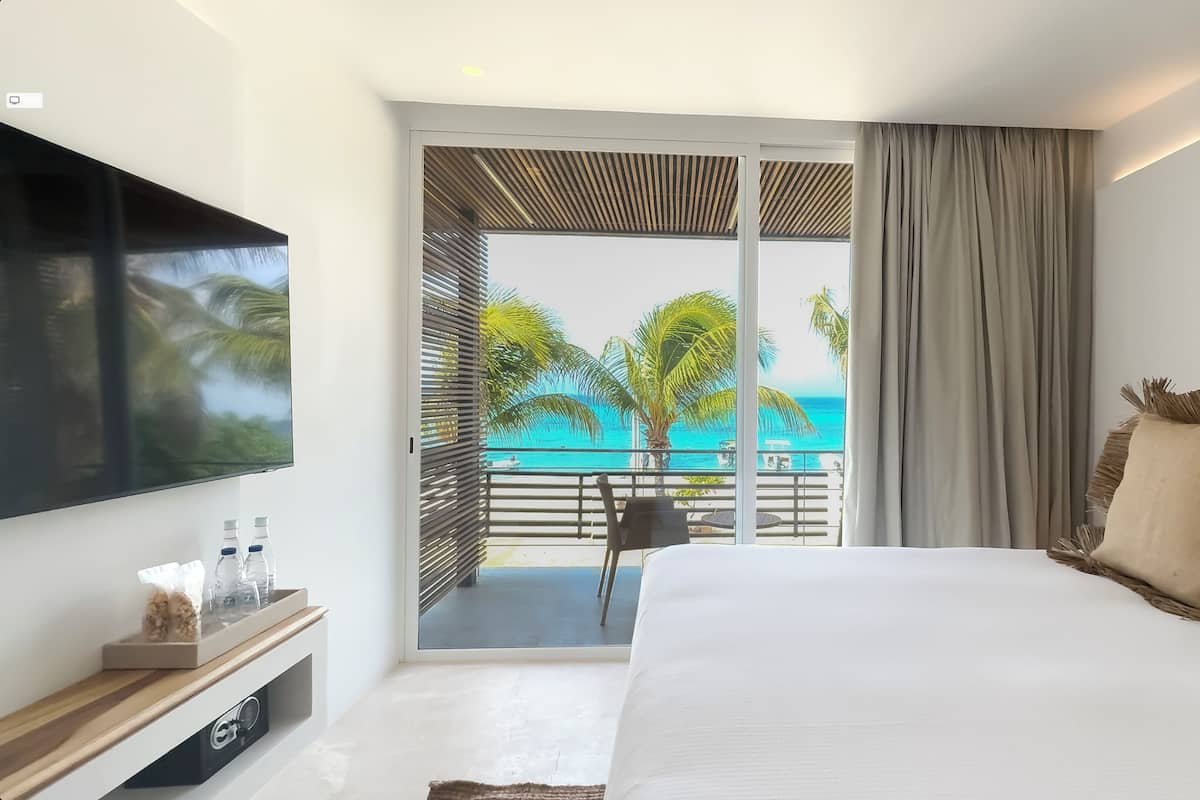 Ein modernes Hotelzimmer mit einem großen Bett, einem Flachbildfernseher, einem Balkon mit Meerblick und einer kleinen Sitzecke.