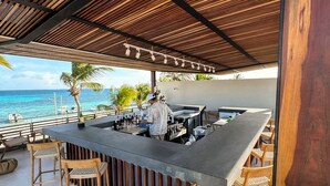 Een terras met een houten overkapping, barstoelen en uitzicht op de oceaan.