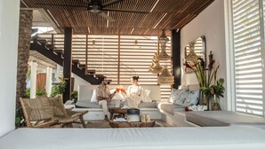 Een moderne woonkamer met een houten plafond, een trap en een groot raam met jaloezieën.
