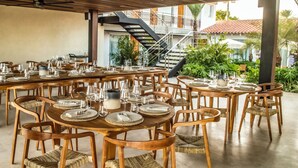 Een restaurant met meerdere ronde tafels, gedekt met borden, glazen en bestek. Er zijn rieten stoelen en een trap die naar een hoger niveau leidt.