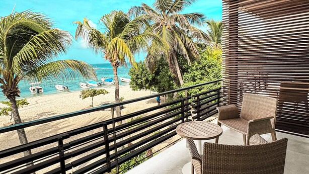 Een balkon met rieten meubilair met uitzicht op een strand met palmbomen en boten.