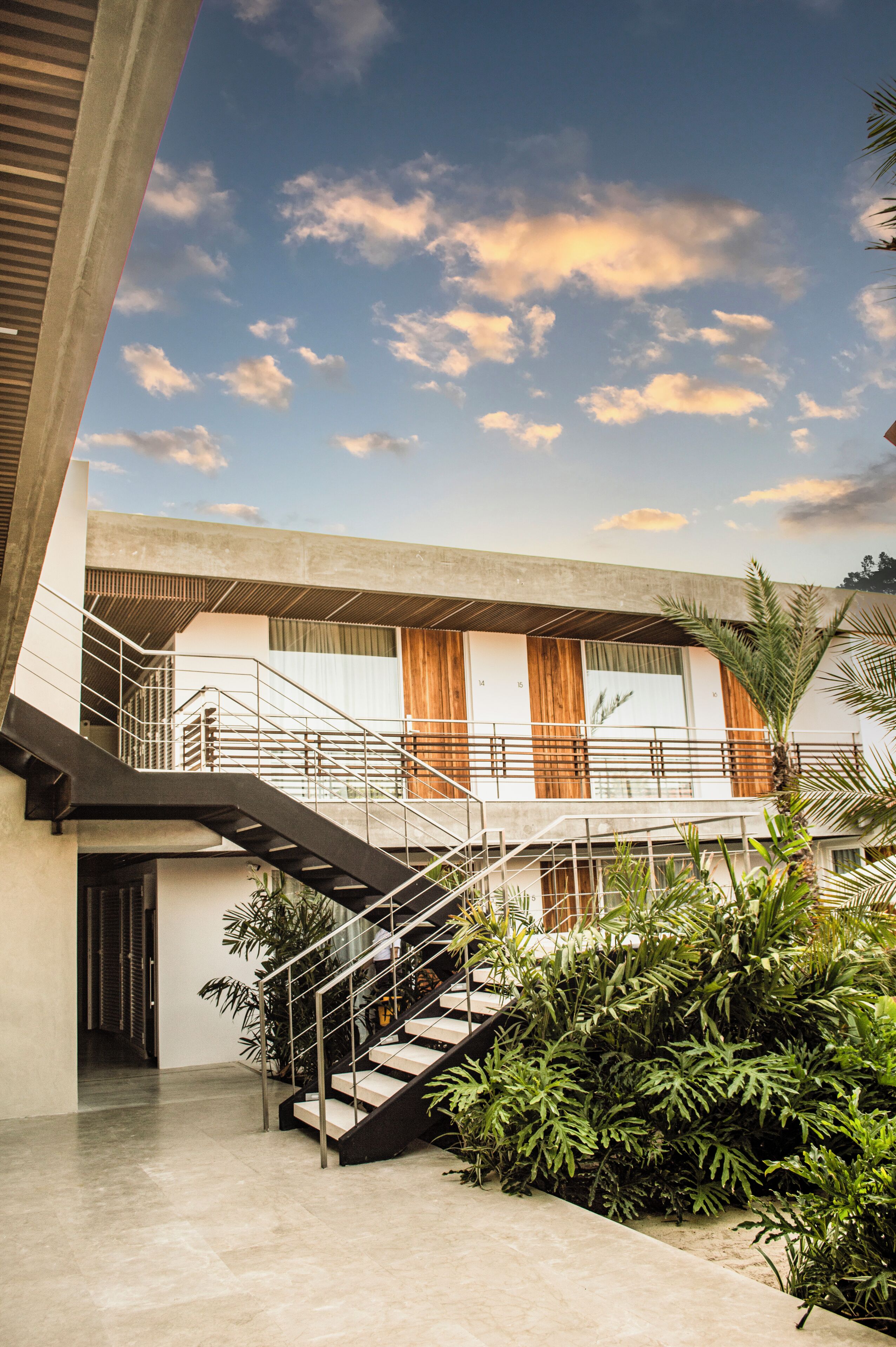 A modern building with a staircase leading to a balcony, surrounded by greenery.