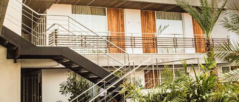 Un bâtiment moderne avec un escalier menant à un balcon, le tout entouré de verdure.