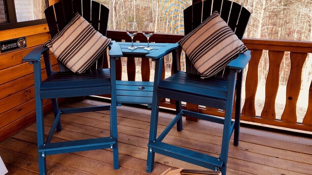 Zwei blaue Adirondack-Stühle mit gestreiften Kissen auf einer Holzterrasse mit Blick auf Bäume.