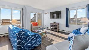 Un salon spacieux doté d’une grande fenêtre, d’un téléviseur à écran plat et d’un coin salon confortable agrémenté de coussins à motifs.
