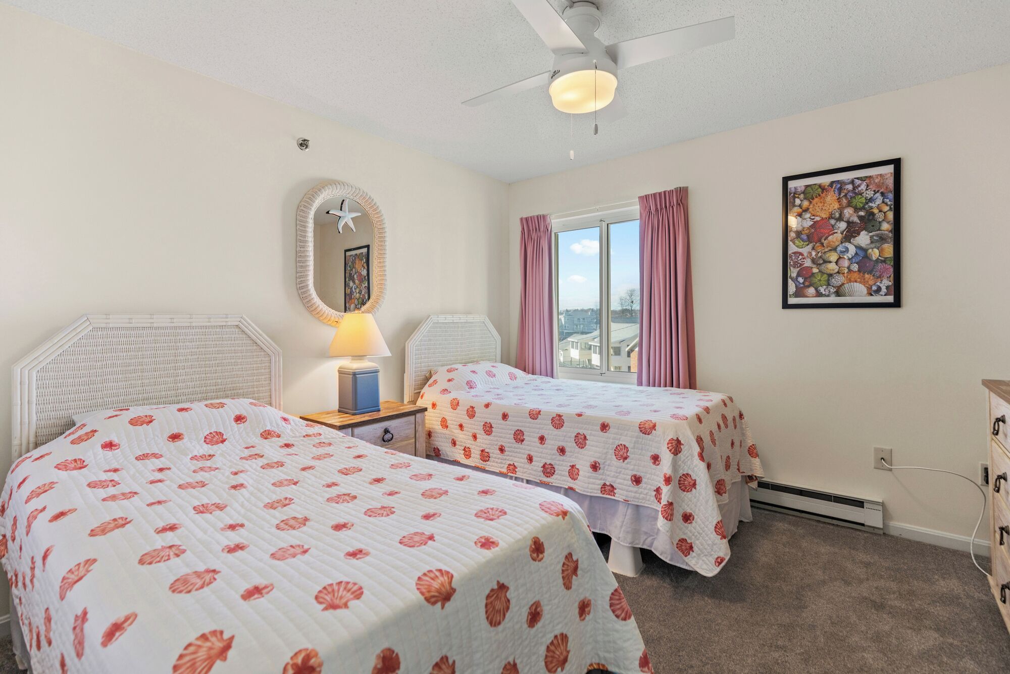 A bedroom with two beds, a ceiling fan, a window with curtains, and a framed picture on the wall.