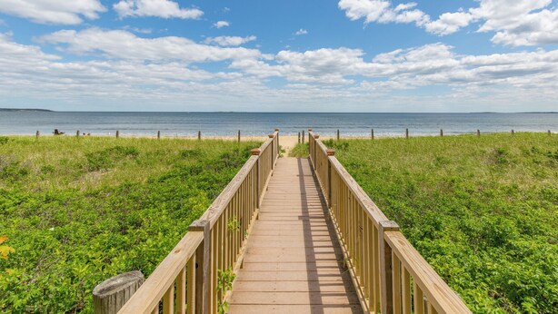 Une promenade en bois menant à une plage, avec un ciel dégagé et une vue sur l’océan.