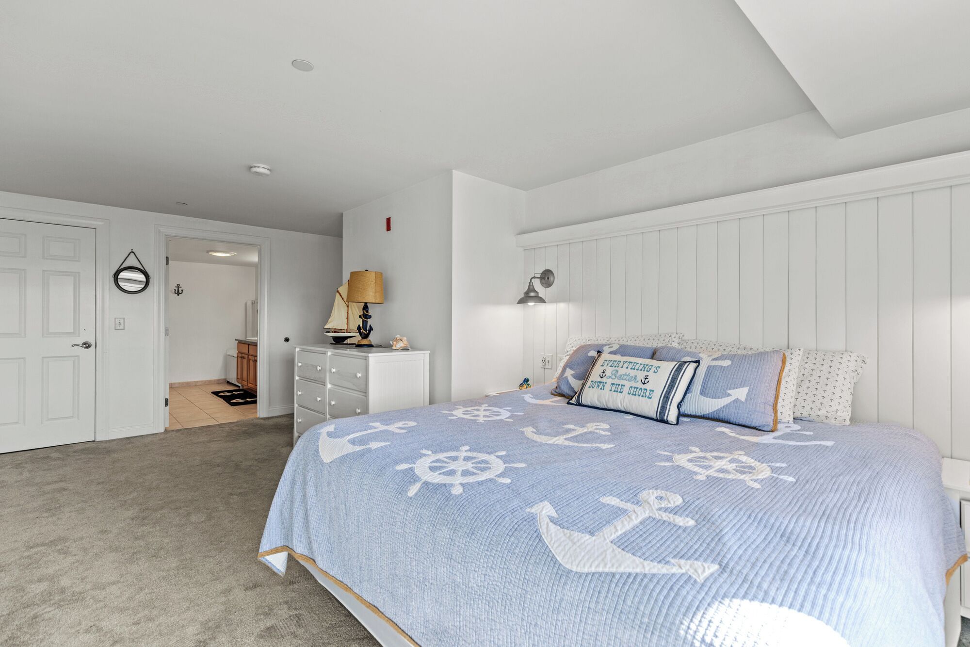 A bedroom with a bed featuring nautical-themed bedding, a dresser, a lamp, and a wall-mounted light fixture.