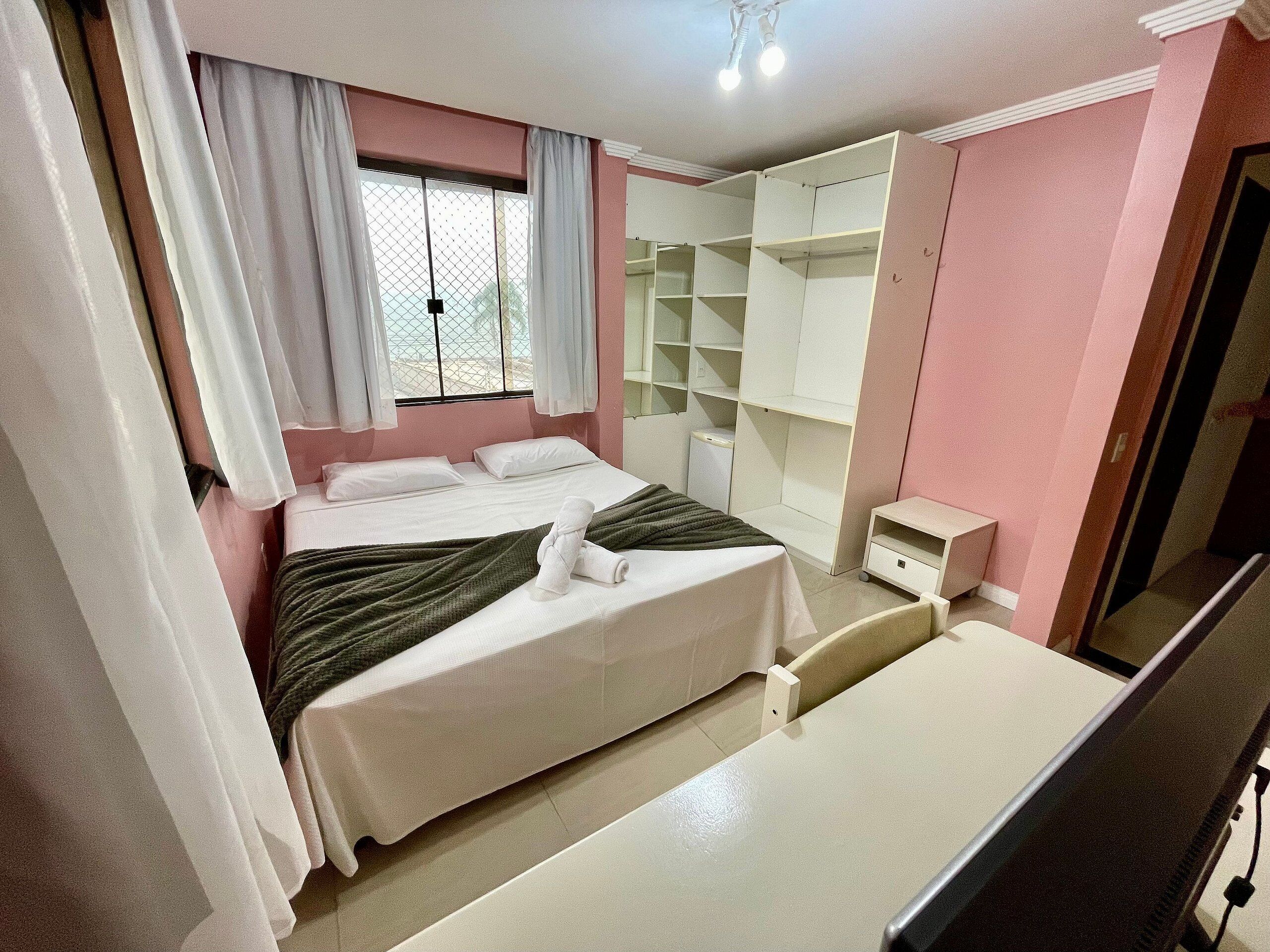 A neatly arranged bedroom with a bed, a bedside table, a wardrobe, and a window with curtains.