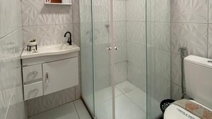 Een moderne badkamer met een douchecabine van glas, een witte wastafel met spiegel erboven en een toilet met decoratieve afdekking.