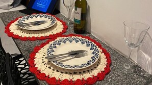 Een eettafel met twee gehaakte tafelonderzetters, een fles wijn en een laptop.