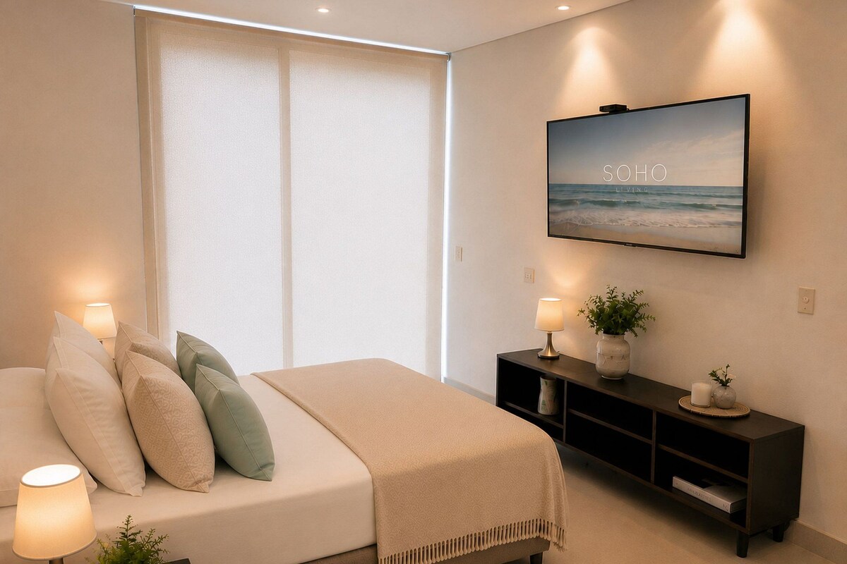 Een slaapkamer met een bed, bedlampjes, een televisie, een console en een raam met zonwering.