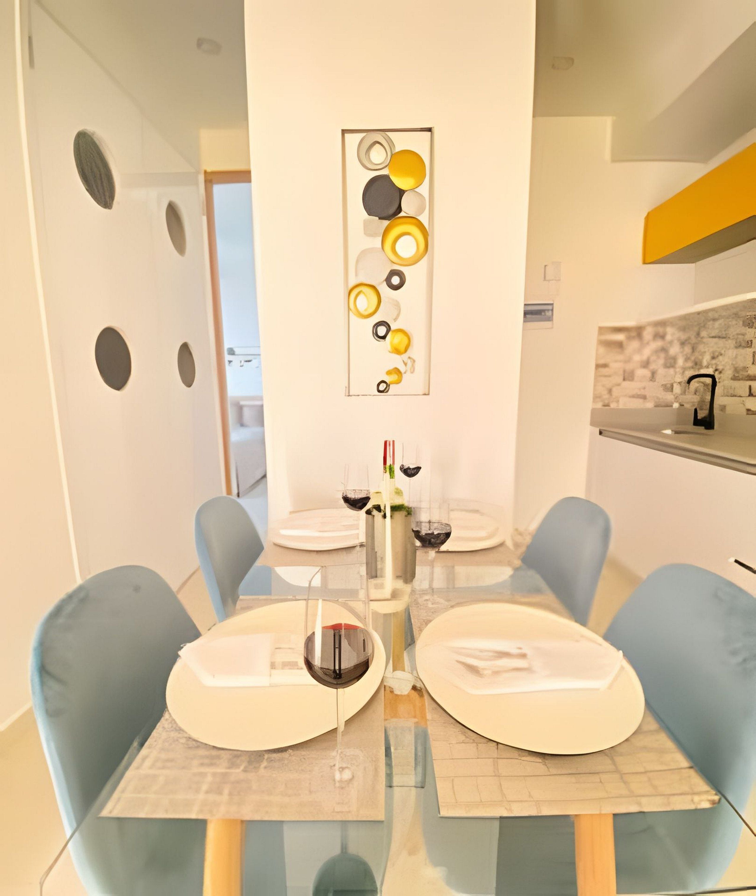 Een moderne eethoek met een glazen tafel, blauwe stoelen en een decoratief kunstwerk erboven.