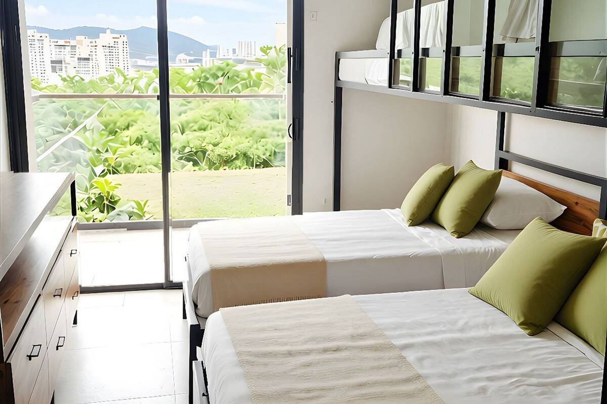 Een hotelkamer met twee bedden, een dressoir, een raam met uitzicht op de stad en een plafondventilator.