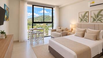 Une chambre d’hôtel avec un grand lit, un canapé, un bureau avec des tabourets et une vue sur l’extérieur.