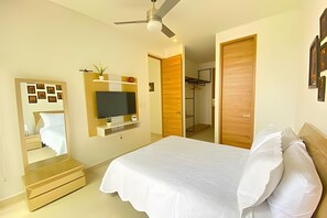 Un dormitorio con una cama, un televisor montado en la pared, un ventilador de techo y una puerta de madera.