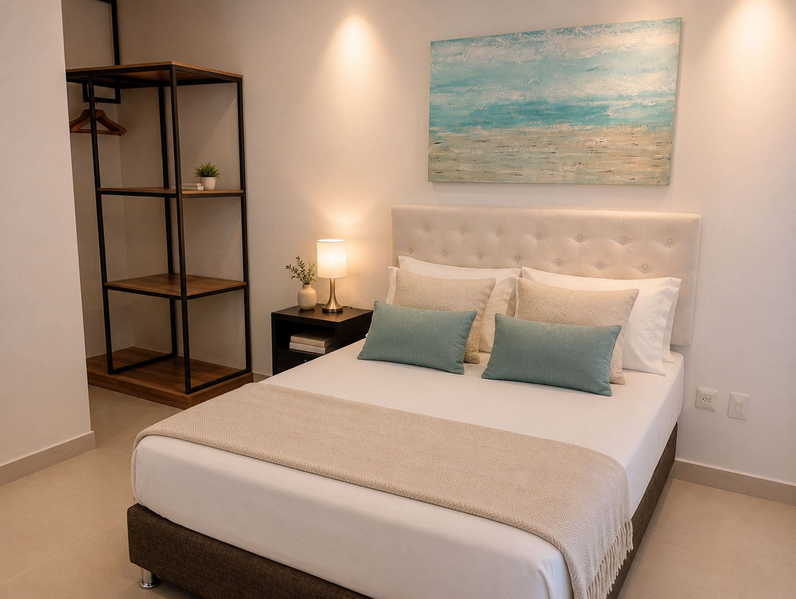 Un dormitorio ordenado con cama, una mesita de noche, un estante en la pared y un cuadro.