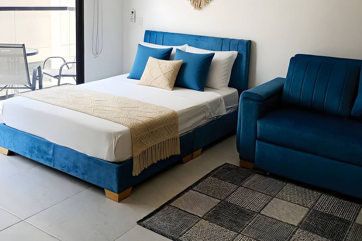 Een moderne slaapkamer met een bed, een blauwe bank, wanddecoratie van macramé en uitzicht door een glazen deur.