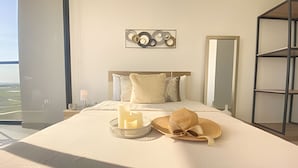 Ein Hotelzimmer mit einem großen Bett, einem Nachttisch mit Lampe, einem Wandbild, einem Spiegel und Blick ins Freie.