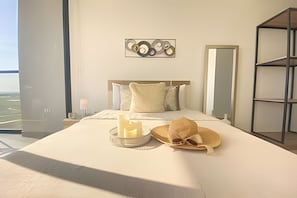 Ein Hotelzimmer mit einem großen Bett, einem Nachttisch mit Lampe, einem Wandbild, einem Spiegel und Blick ins Freie.