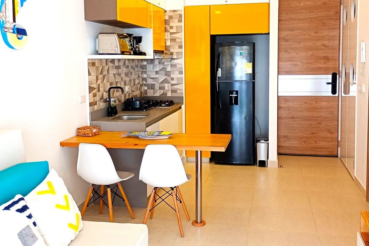 A compact kitchen with a modern black refrigerator, a small dining area with two chairs, and a wooden table.