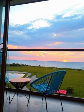Un balcon offrant une vue sur le coucher de soleil sur l’océan, avec une table et deux chaises.