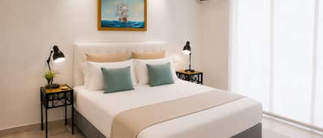 A bedroom with a large bed, two bedside tables with lamps, a painting on the wall, and an air conditioning unit.
