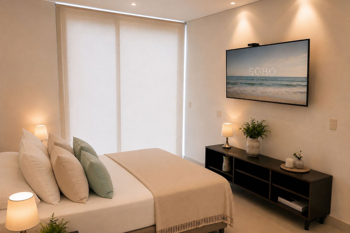 Een slaapkamer met een bed, bedlampjes, een televisie, een console en een raam met zonwering.