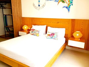 Een netjes opgemaakt bed met een houten hoofdbord, twee nachtkastjes met lampen en een kleurrijk kussen.