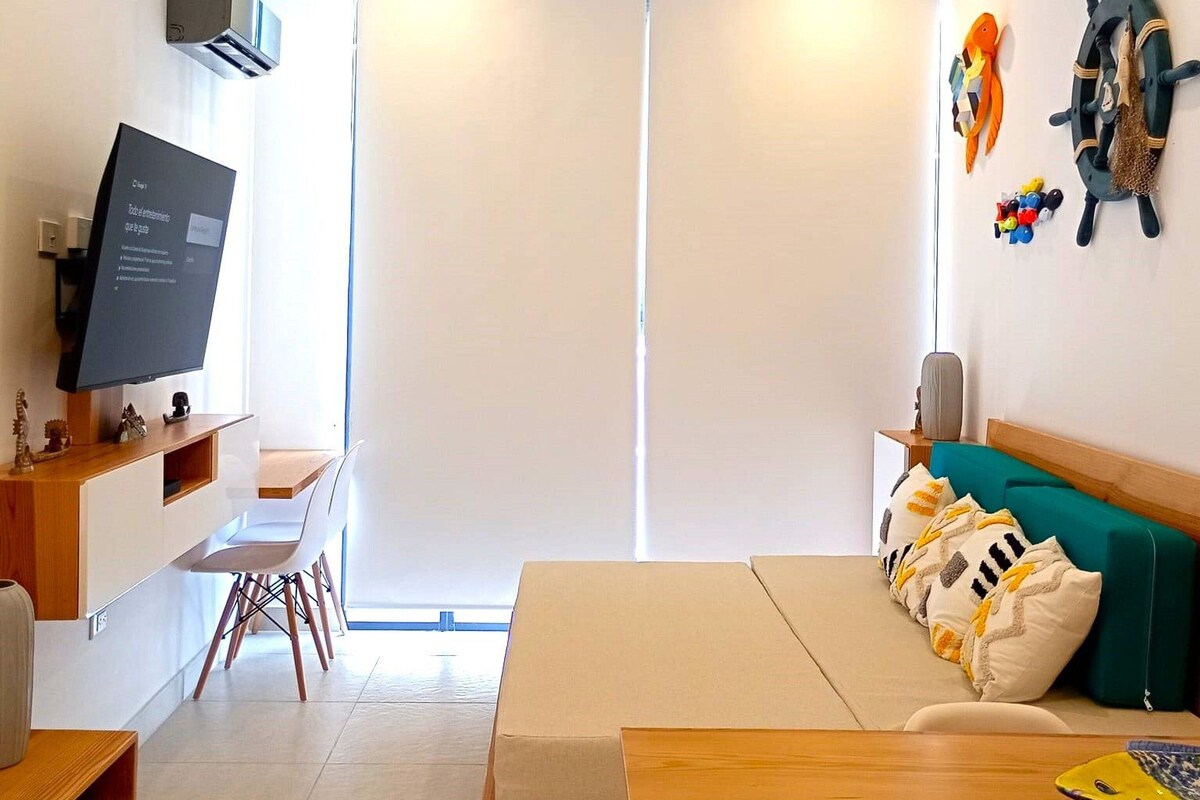 Een moderne woonkamer met een flatscreen televisie, een houten tafel, een groene bank en een schuifpui naar een balkon.
