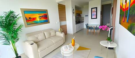 Een moderne woonkamer met een beige bank, een blauwe fauteuil, een salontafel en een eethoek met tafel en stoelen.