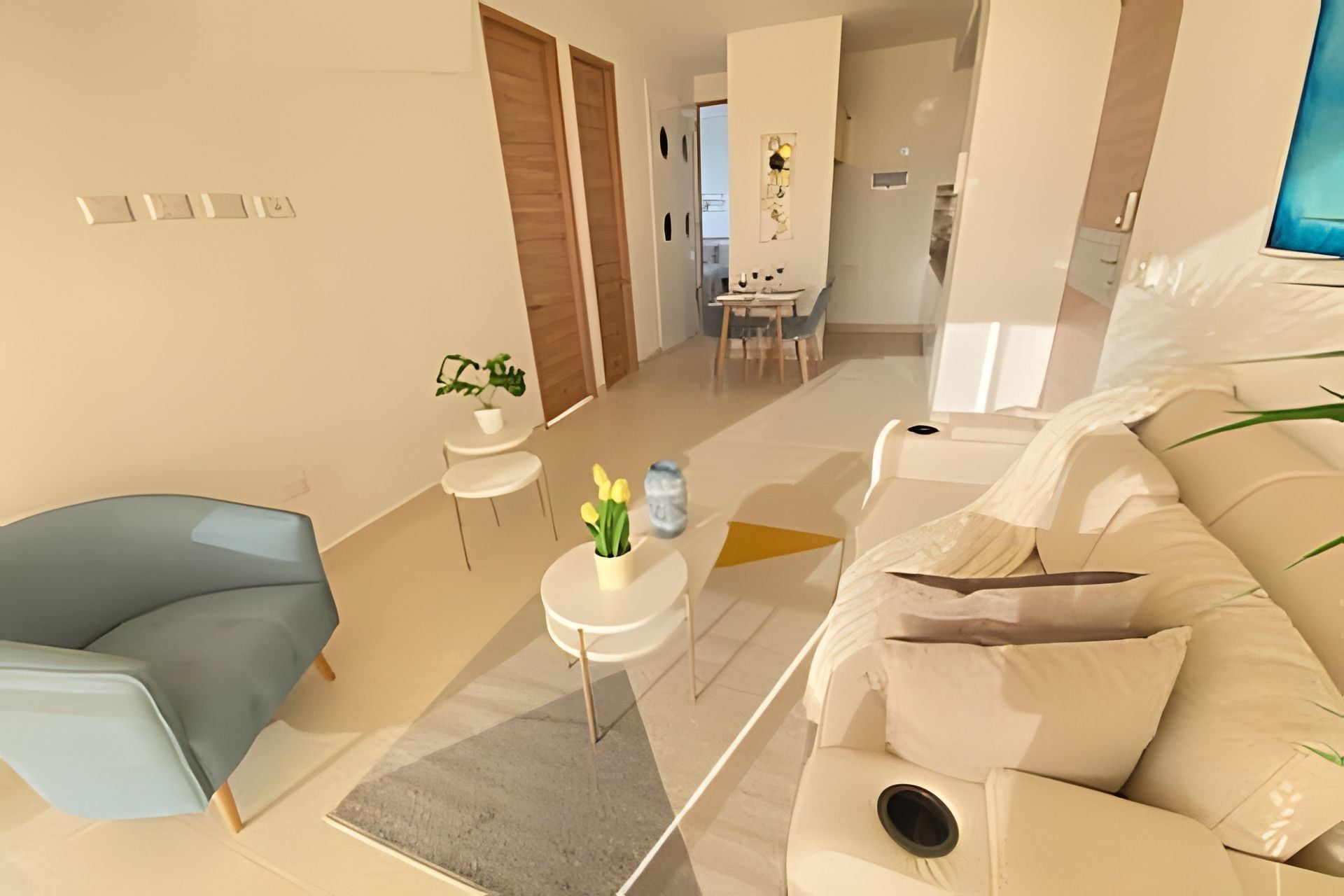 A modern living room with a blue armchair, a white sofa, a small round table with a vase of yellow flowers, and a grey rug.