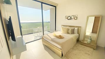 Un dormitorio moderno con una cama grande, una mesita de noche, un espejo y vistas al exterior a través de un ventanal corredero.