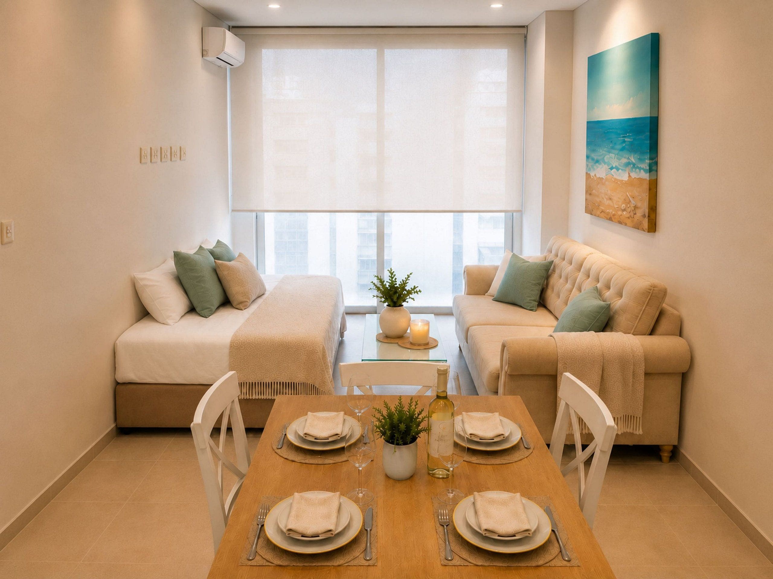 A modern living room with a dining table set for two, a sofa, and a large window with blinds.