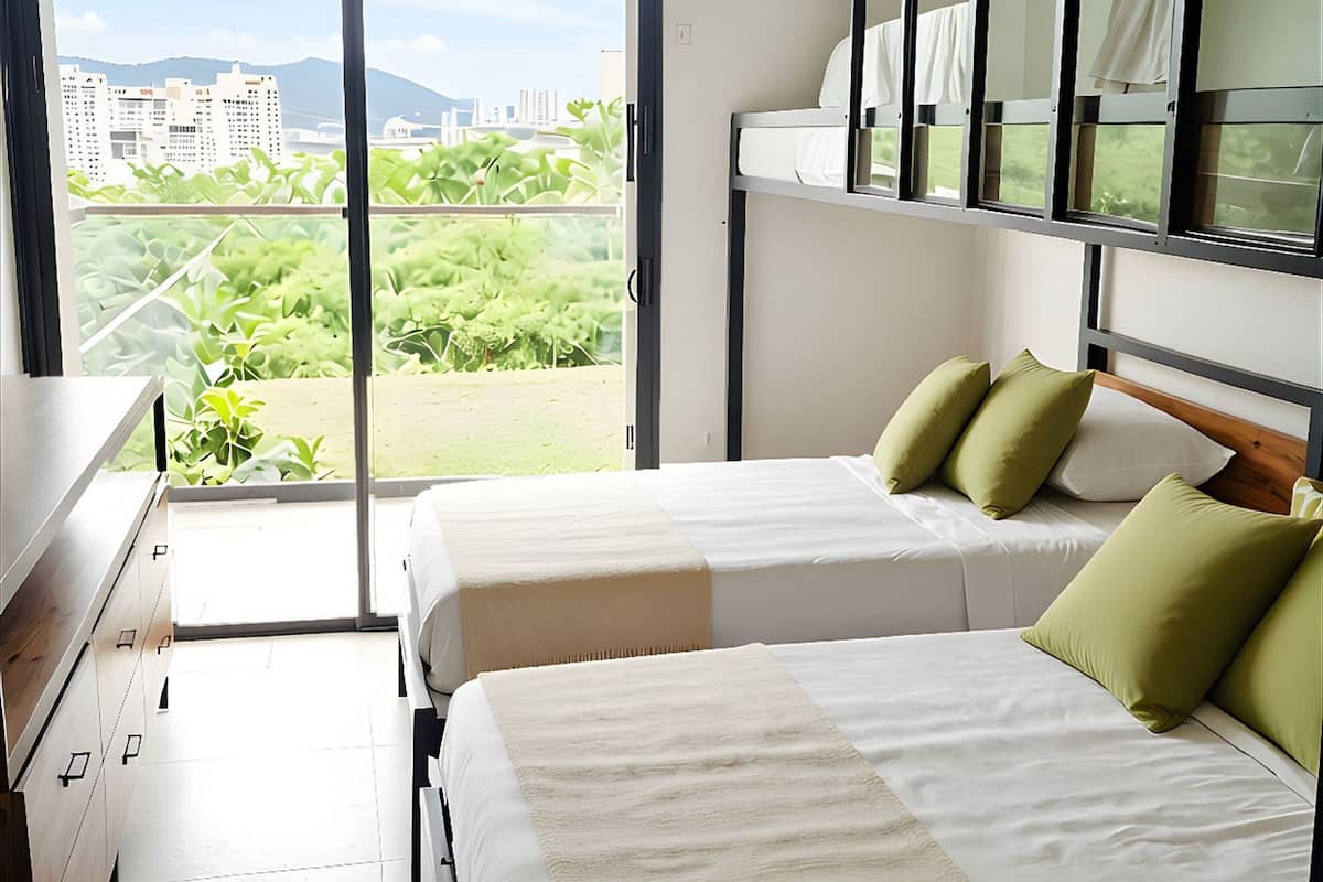 Une chambre d’hôtel avec deux lits, une commode, une fenêtre donnant sur la ville et un ventilateur de plafond.