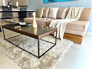 Un salon avec une table basse en verre, un canapé beige et un tapis à poils longs blanc.