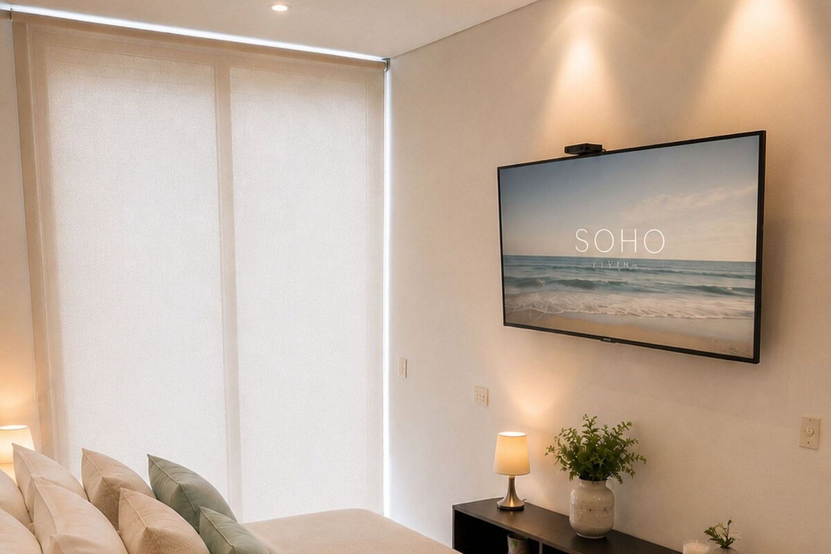 Een moderne slaapkamer met een bed, bedlampen, een televisie en een console met decoratieve objecten.