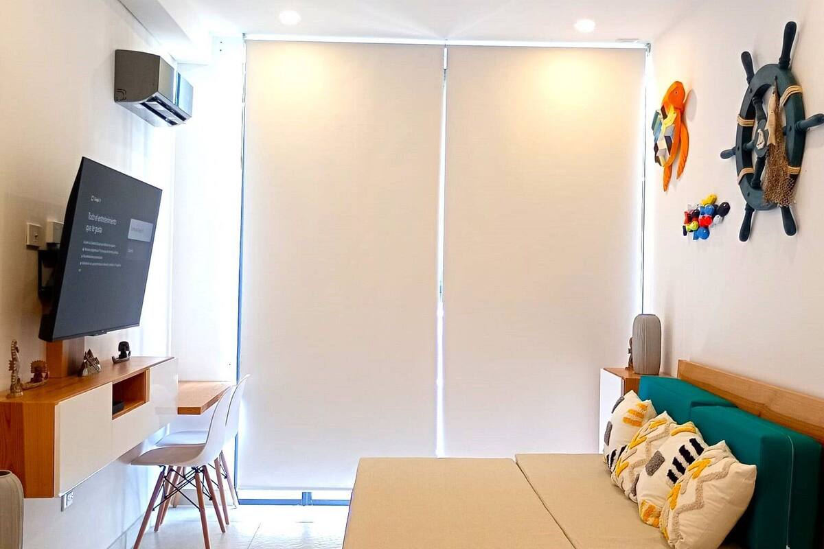 Een moderne woonkamer met een flatscreen televisie, een houten tafel, een groene bank en een schuifpui naar een balkon.