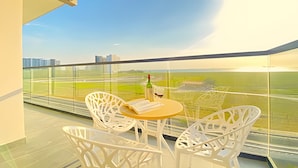 Een balkon met witte rieten stoelen en een klein, rond tafeltje, met uitzicht op een stadsbeeld en akkers.