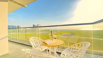 Un balcon avec des fauteuils en osier blanc et une petite table ronde, d’où l’on peut admirer le paysage urbain et les champs environnants.