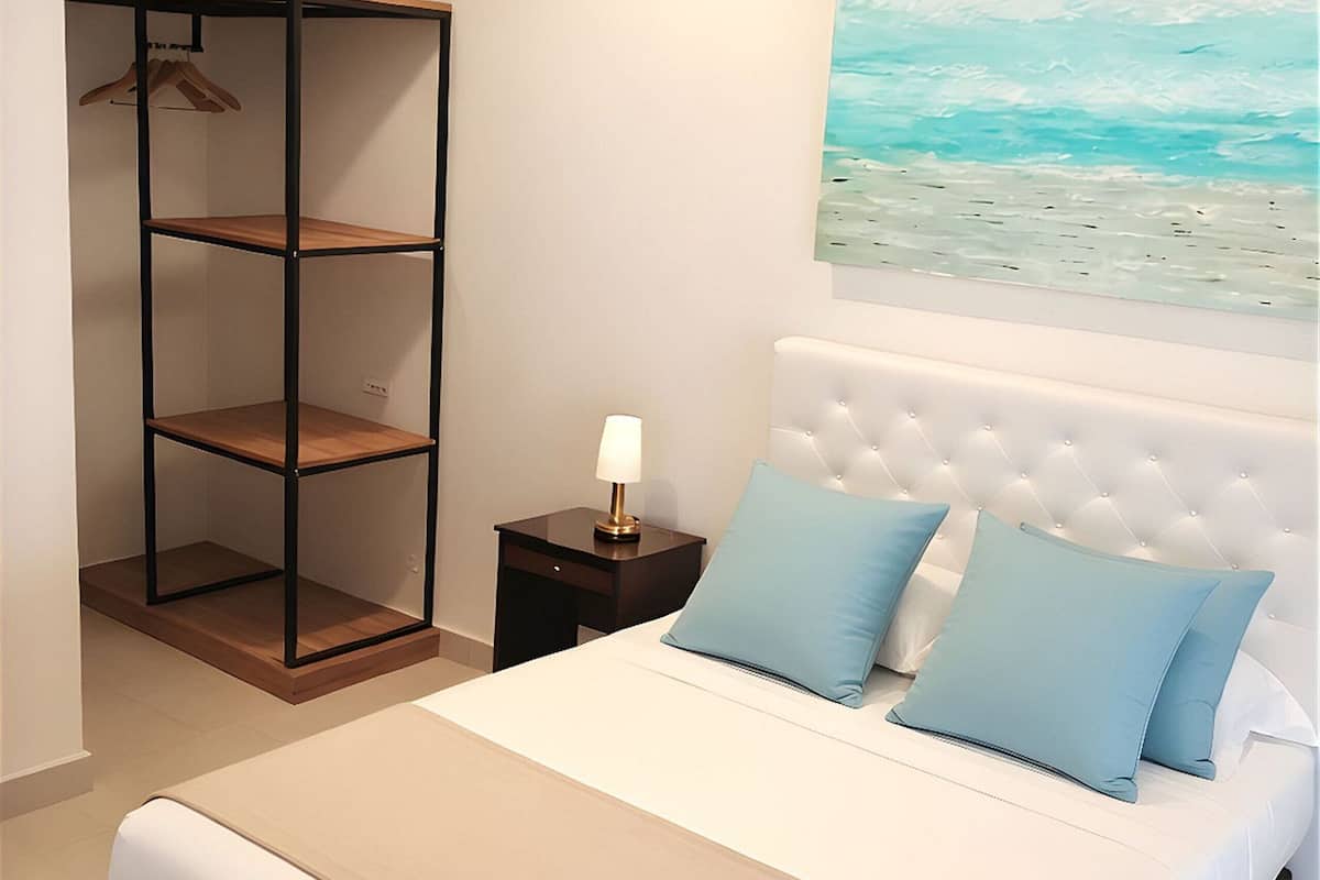 Une chambre à coucher comprenant un lit, une table de chevet, une étagère fixée au mur et un tableau.