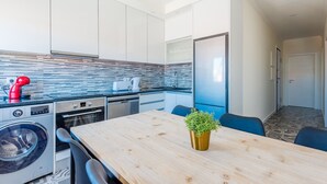 A compact kitchen with modern appliances, a wooden dining table, and a small potted plant. - Bela Vista C in Lisboa (Lisboa ciudad)