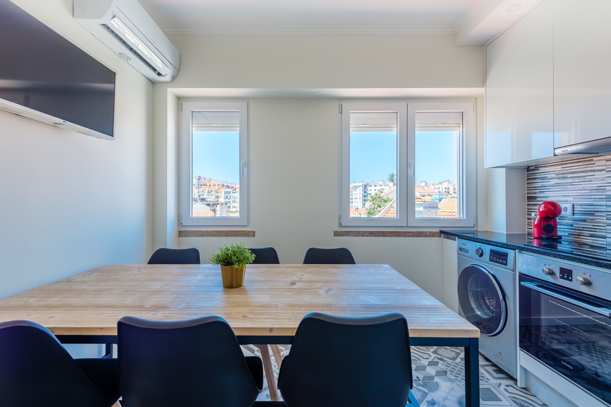 A modern kitchen with a washing machine, oven, and a dining area with a table and chairs.