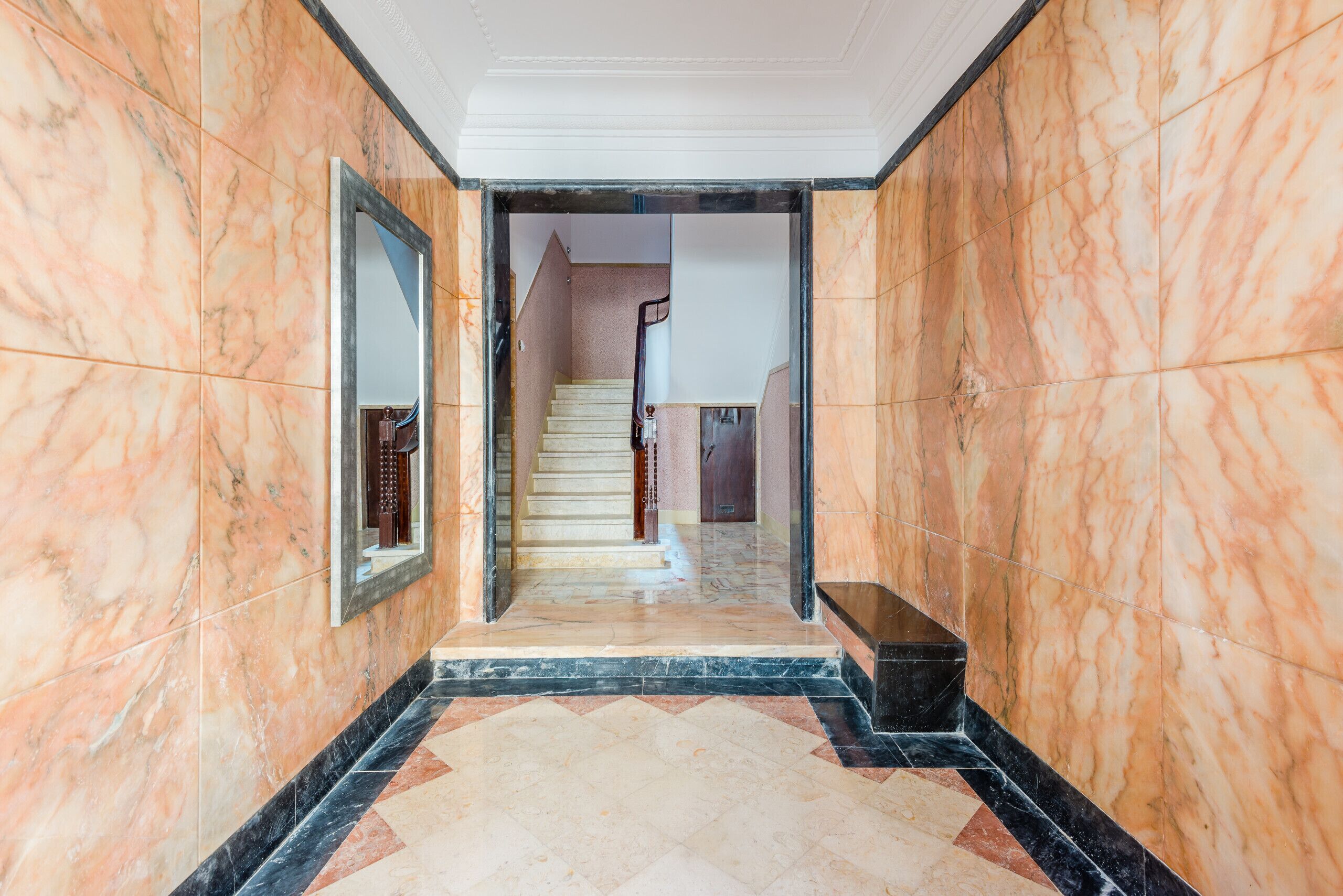 Um corredor de mármore com escadaria que dá para um andar superior.