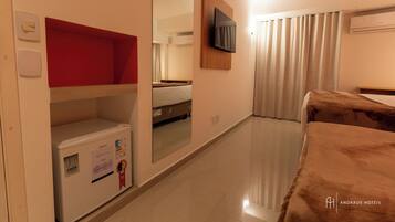 A hotel room with a bed, a television mounted on the wall, a wardrobe, and a mirror reflecting the room.