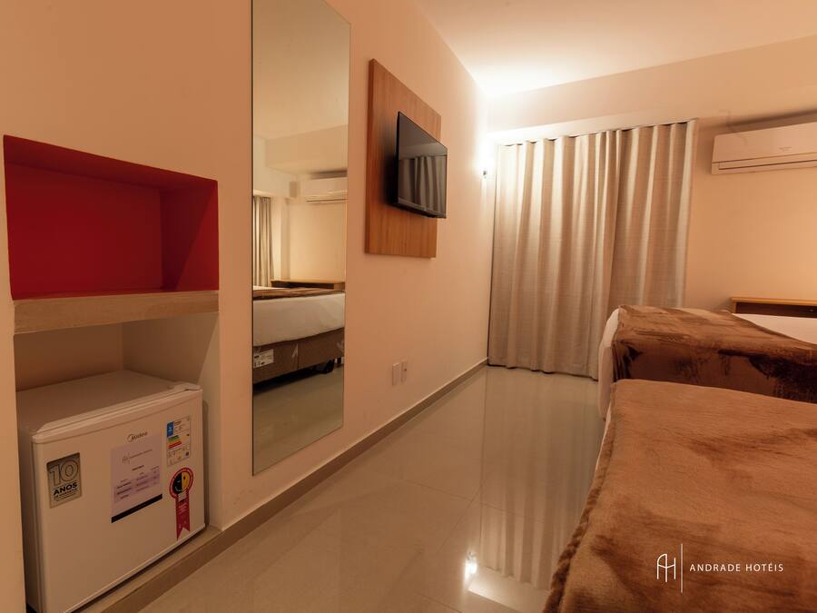 A hotel room with a bed, a television mounted on the wall, a wardrobe, and a mirror reflecting the room.