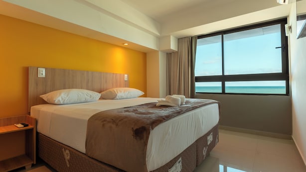 Una camera d'albergo con un letto, un comodino, una finestra vista mare e una lampada a soffitto.
