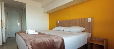 Una habitación de hotel con una cama, cabecera de madera, manta marrón y toalla blanca.
