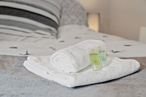 Ein ordentlich gefaltetes weißes Handtuch und eine Flasche Duschgel auf einem Bett mit gemustertem Überwurf.